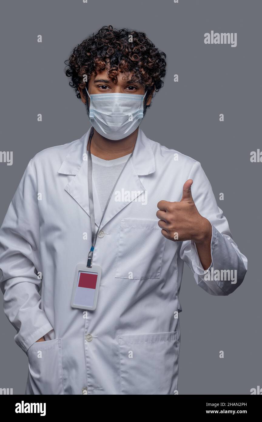 Medico di sesso maschile in faccia che copre mostrando un segno di approvazione Foto Stock