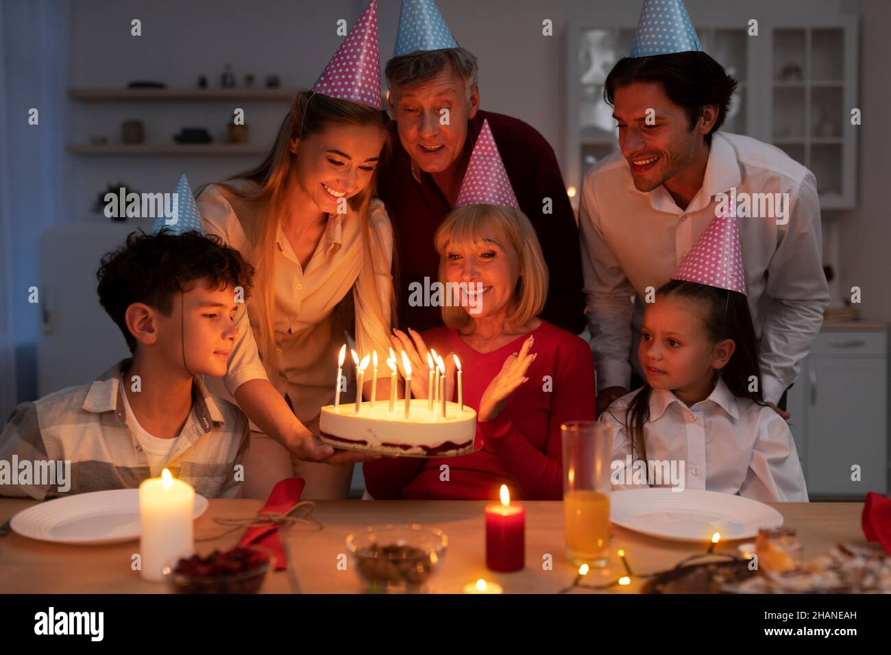Felice famiglia multi generazione che ha festa di compleanno, dando torta con candele accese a donna anziana, congratulandosi con lei Foto Stock