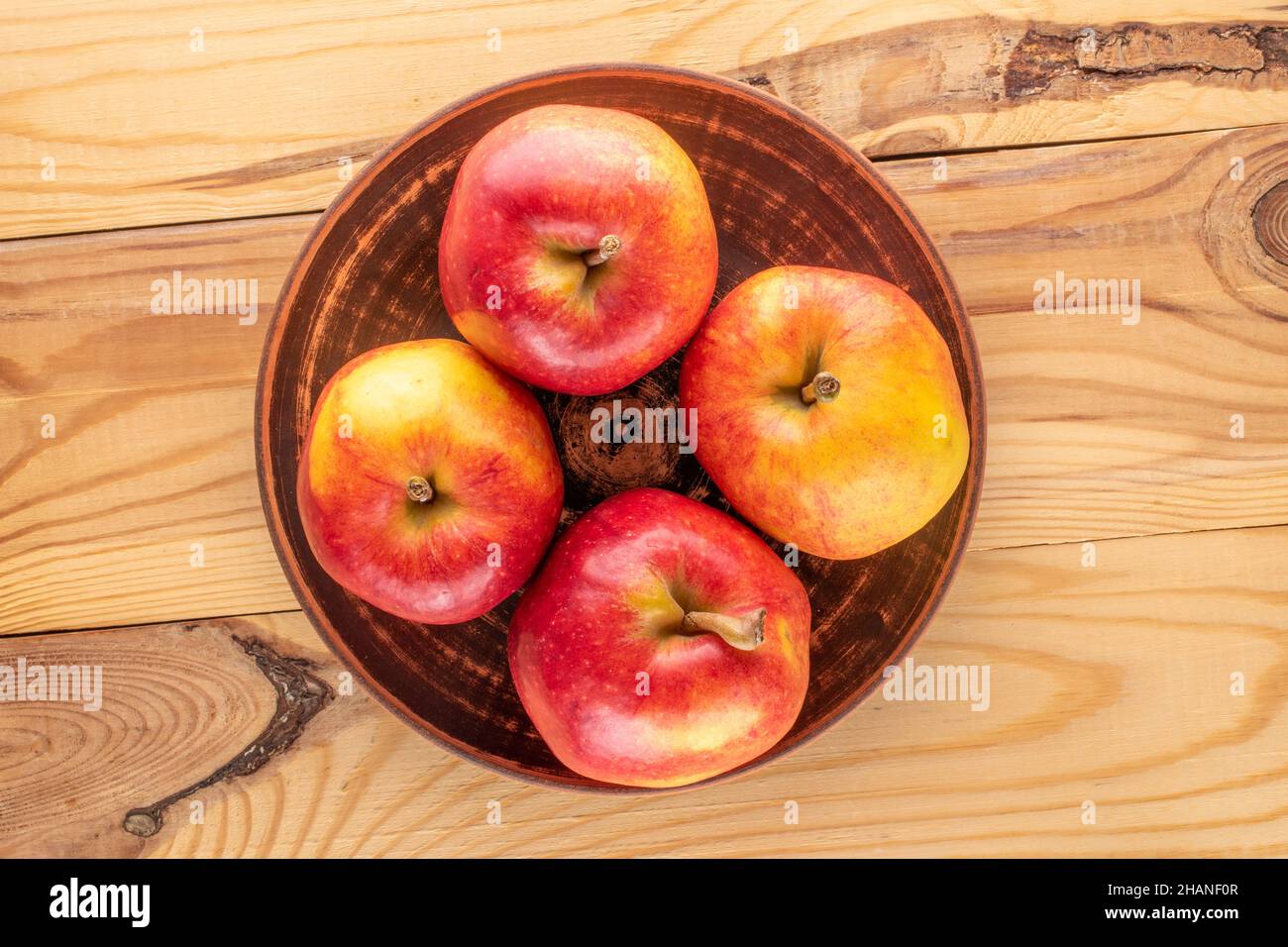 Quattro mele rosse dolci in un piatto di argilla su un tavolo di legno, primo piano, vista dall'alto. Foto Stock