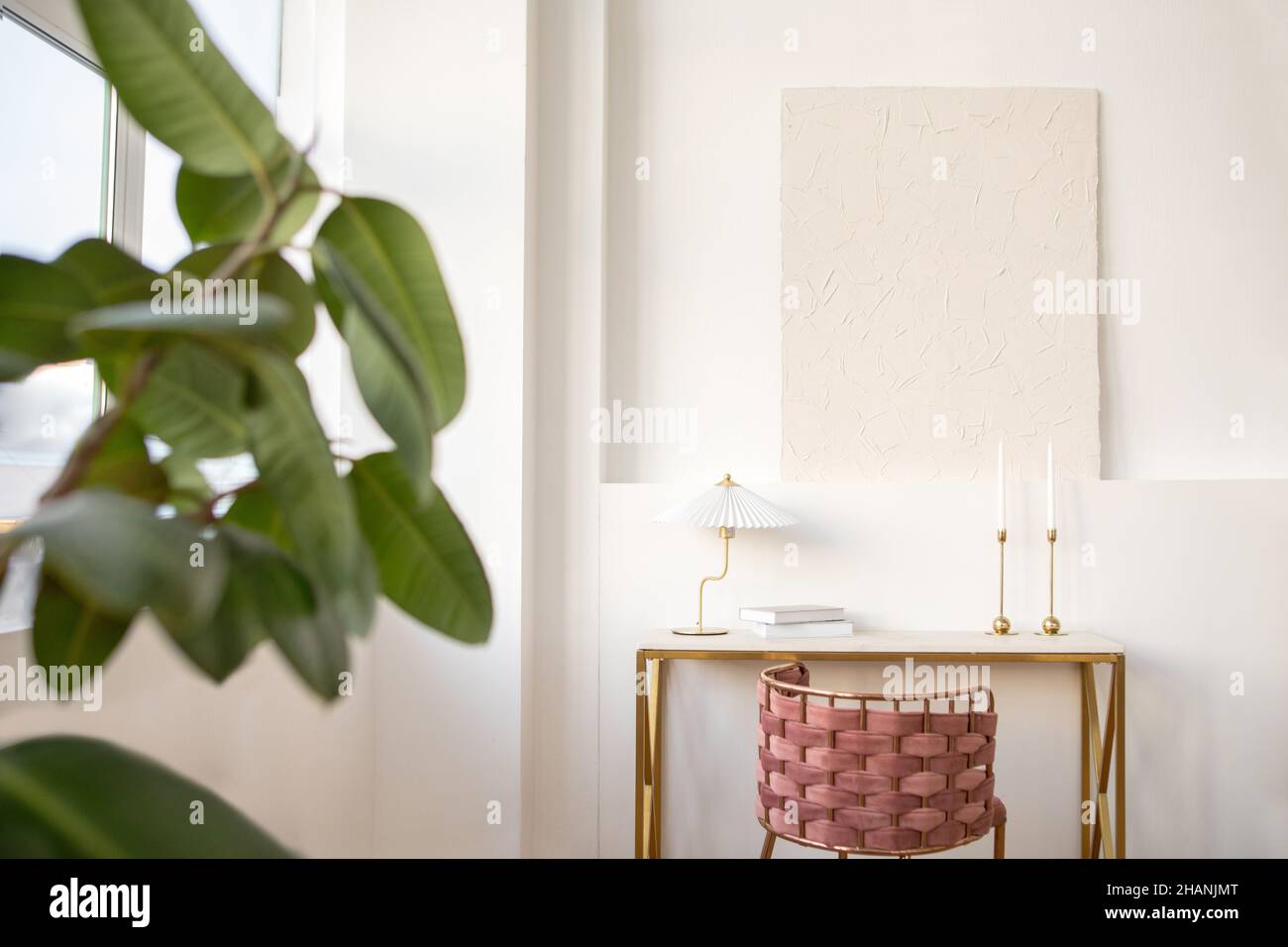 Interni design di stanza luminosa arredato con tavolo con sedia in vimini e lampada e libri posti vicino a parete bianca con sporgenza con pittura bianca su di esso Foto Stock