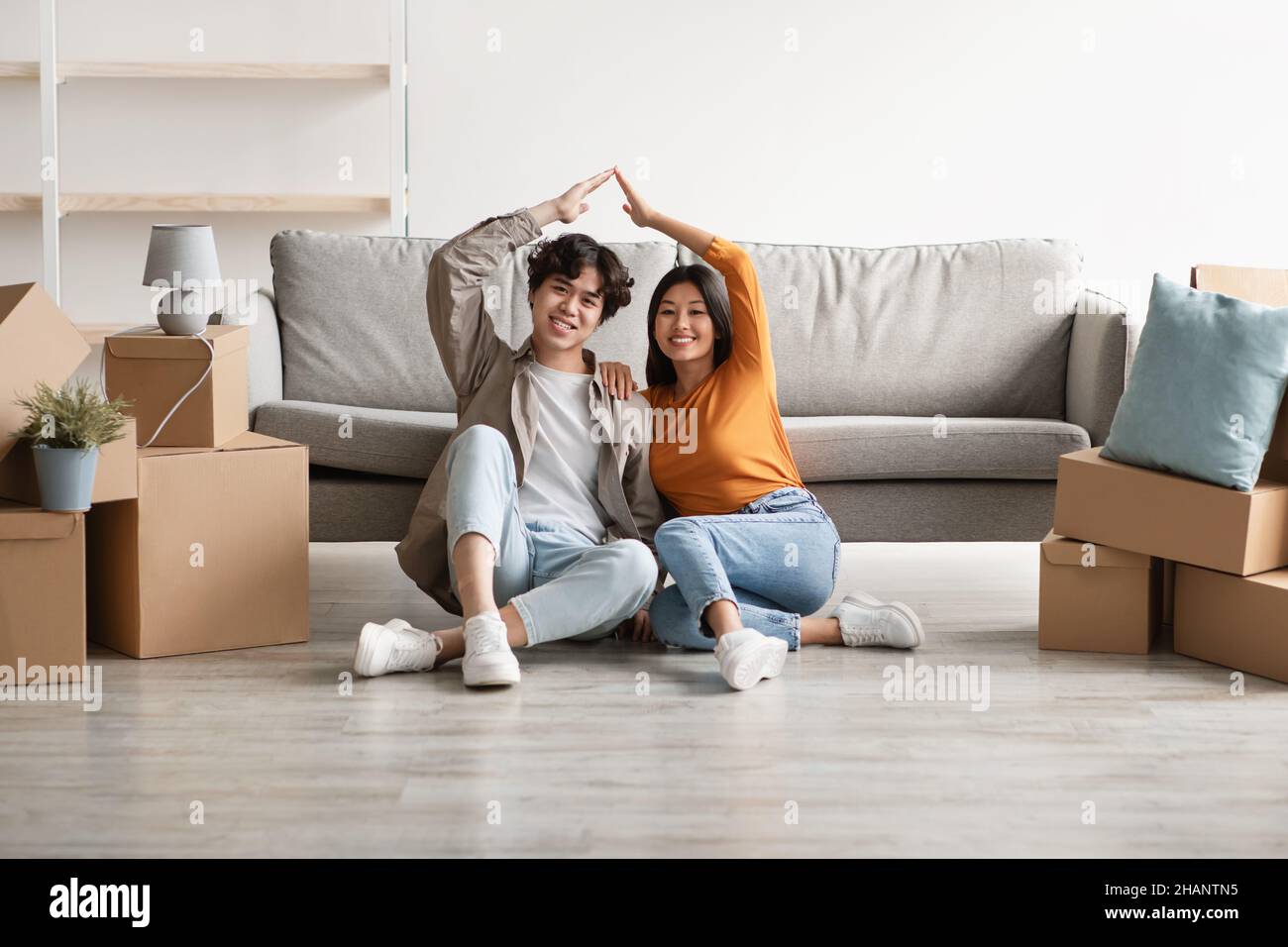 Giorno di trasferimento. Felice giovane coppia asiatica che si sposta a casa propria, unendo le mani, rendendo il tetto della casa gesto insieme Foto Stock