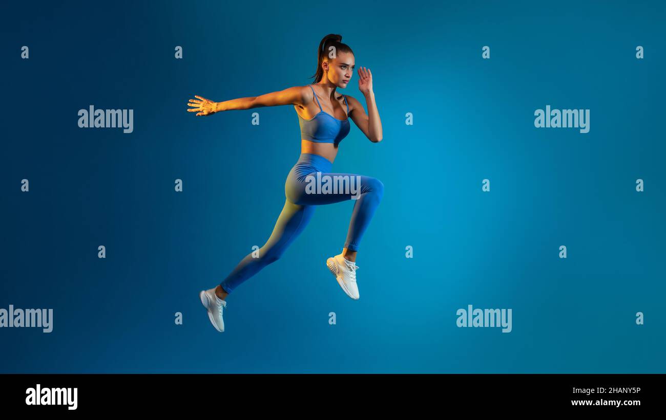 Fitness Donna saltando in aria media su sfondo blu, Panorama, a tutta lunghezza Foto Stock
