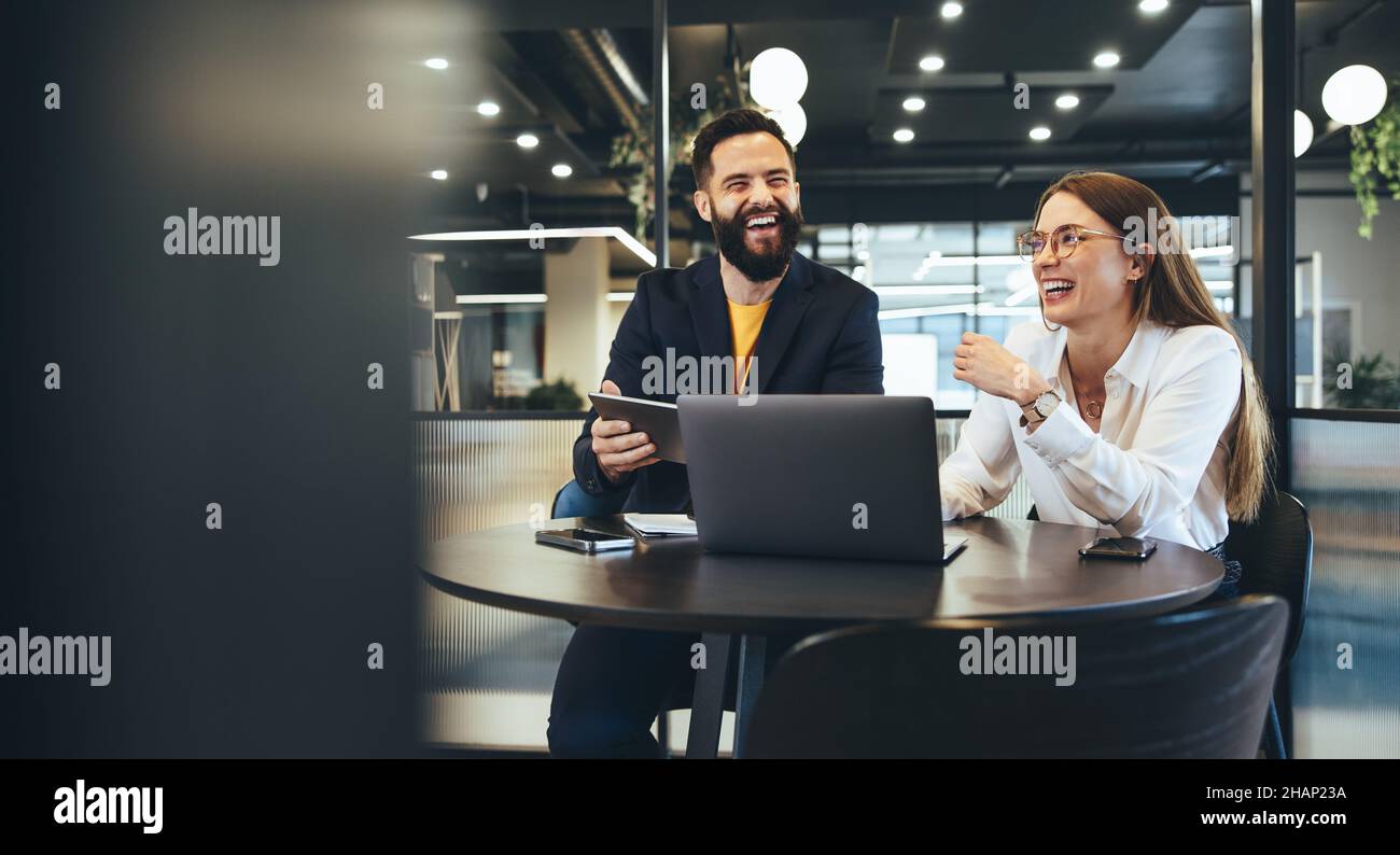 Due giovani uomini d'affari felici che lavorano insieme in uno spazio di lavoro moderno. Due giovani imprenditori sorridono allegro mentre lavorano con la tecnologia wireless Foto Stock