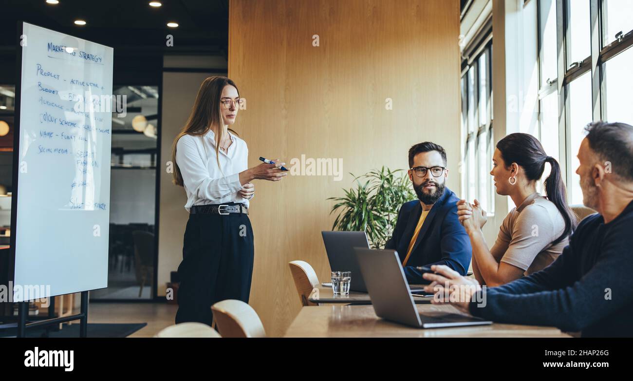 Giovane donna d'affari fiduciosa che discute la sua strategia di marketing e le sue idee con il suo team. Donna manager che fa una presentazione durante un incontro con lui Foto Stock