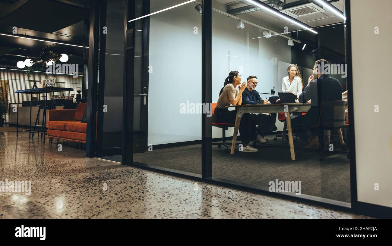 colleghi d'affari che tengono una riunione in una sala riunioni trasparente. Gruppo di professionisti felici che discutono durante un briefing. Diversi Foto Stock