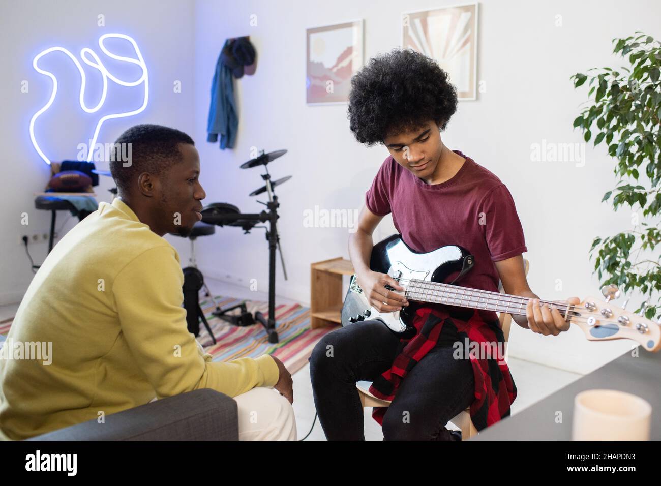Insegnante di musica di etnia africana consulenza ragazzo biraciale con chitarra seduta davanti a lui in ambiente domestico Foto Stock
