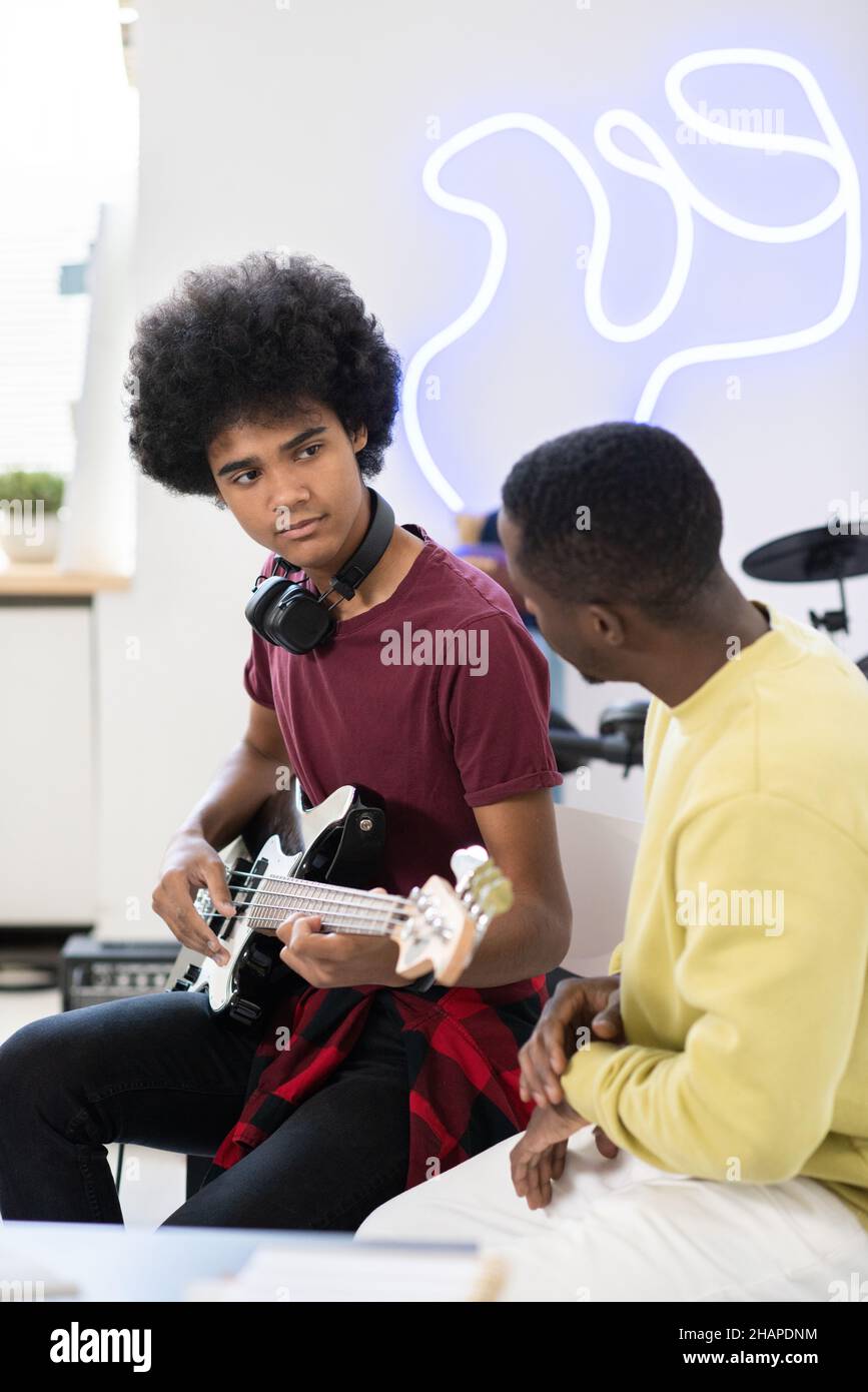 Ragazzo diligente che guarda il suo insegnante di musica mentre si siede di fronte a lui e suona la chitarra a casa lezione Foto Stock
