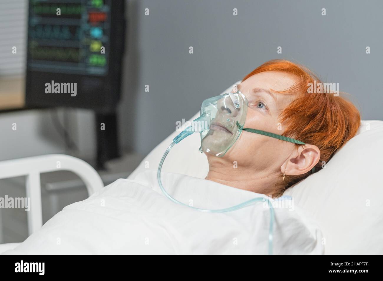 Donna anziana sdraiata nel letto d'ospedale in maschera di ossigeno sul viso, respira duramente durante la malattia Foto Stock