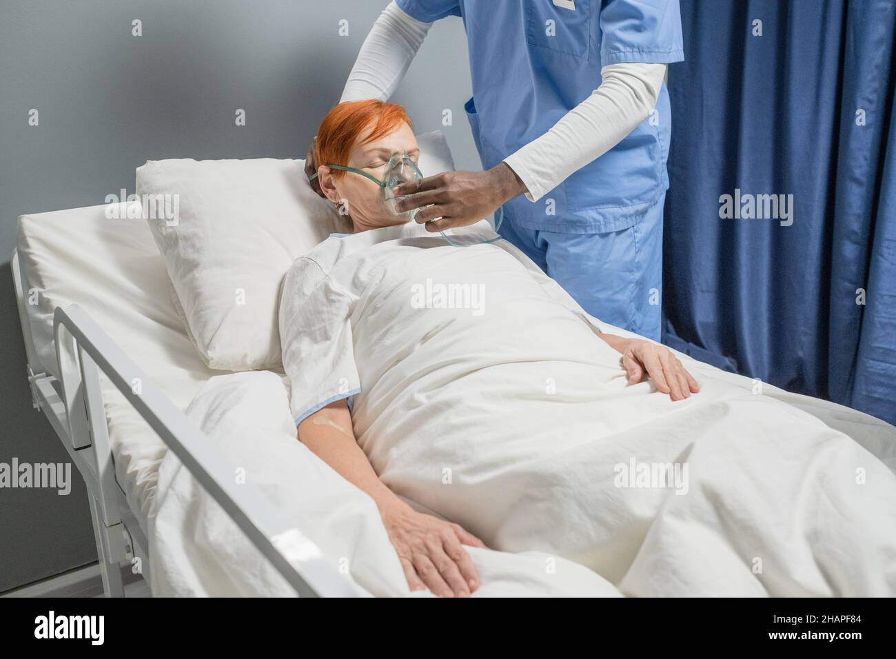 Dottore in uniforme che mette una maschera di ossigeno su un volto di donne anziane, mentre lei si trova a letto in un reparto ospedaliero Foto Stock