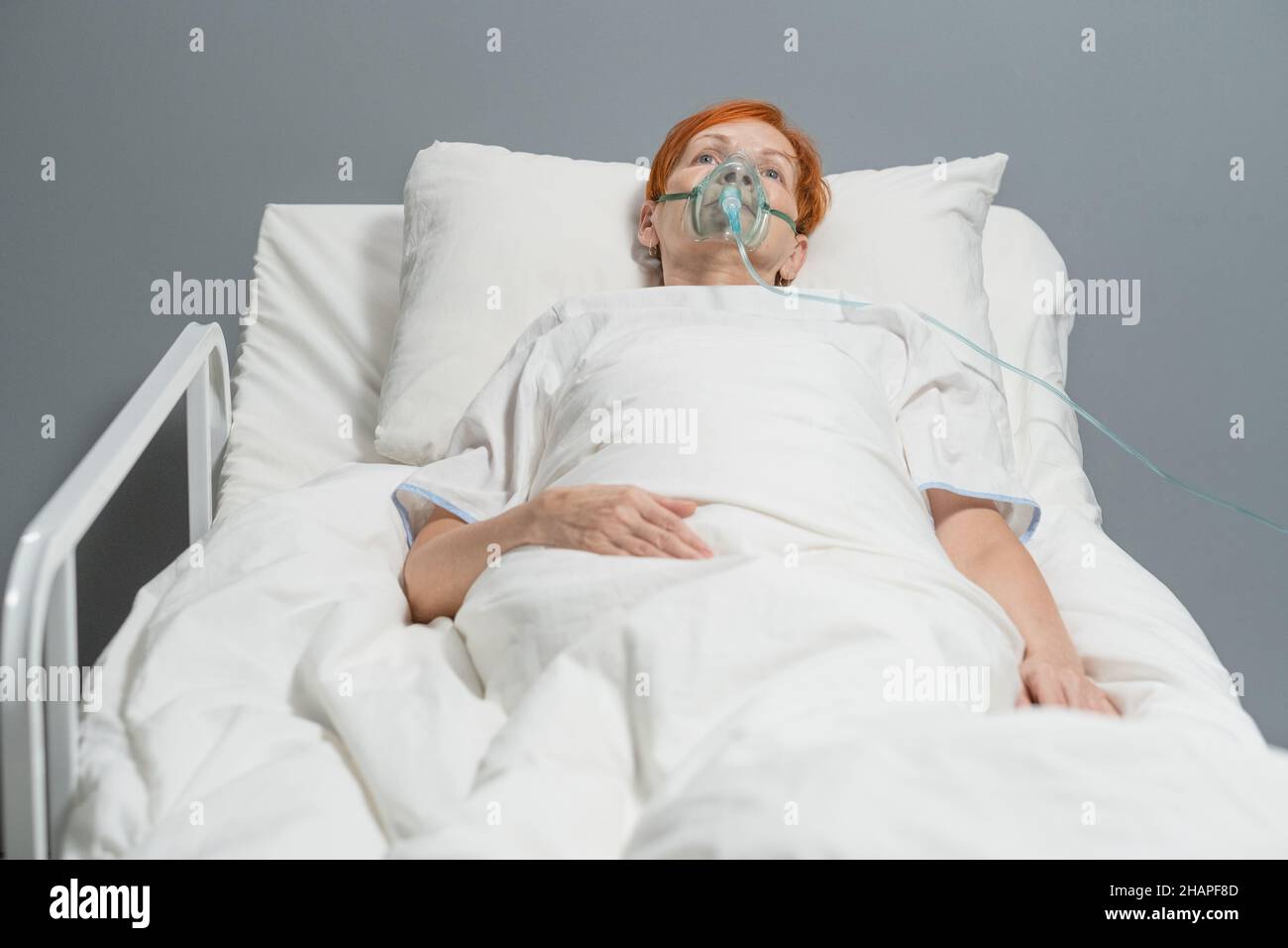 Donna anziana che respira con maschera di ossigeno sul viso mentre si trova a letto presso il reparto ospedaliero Foto Stock