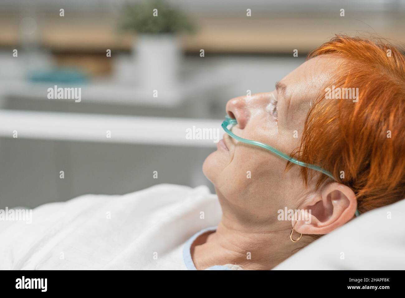 Primo piano di una donna anziana con tubo nel naso per respirare facilmente, si trova a letto in reparto ospedale Foto Stock