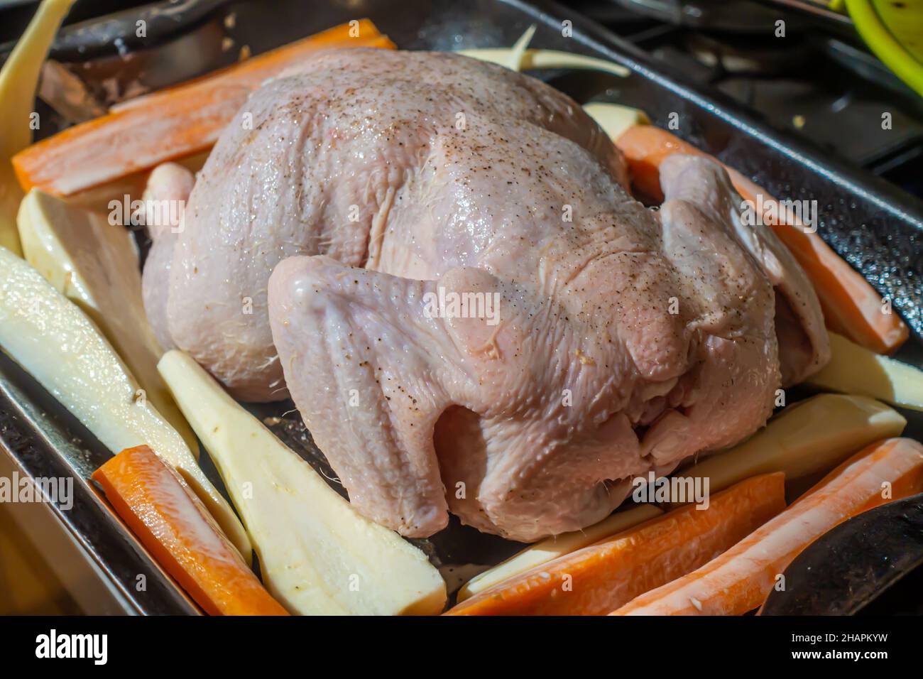Un pollo in una teglia per arrostire preparato e pronto per il forno, dove verrà arrostito con pezzi di pastinaca e carote a fettine. Foto Stock