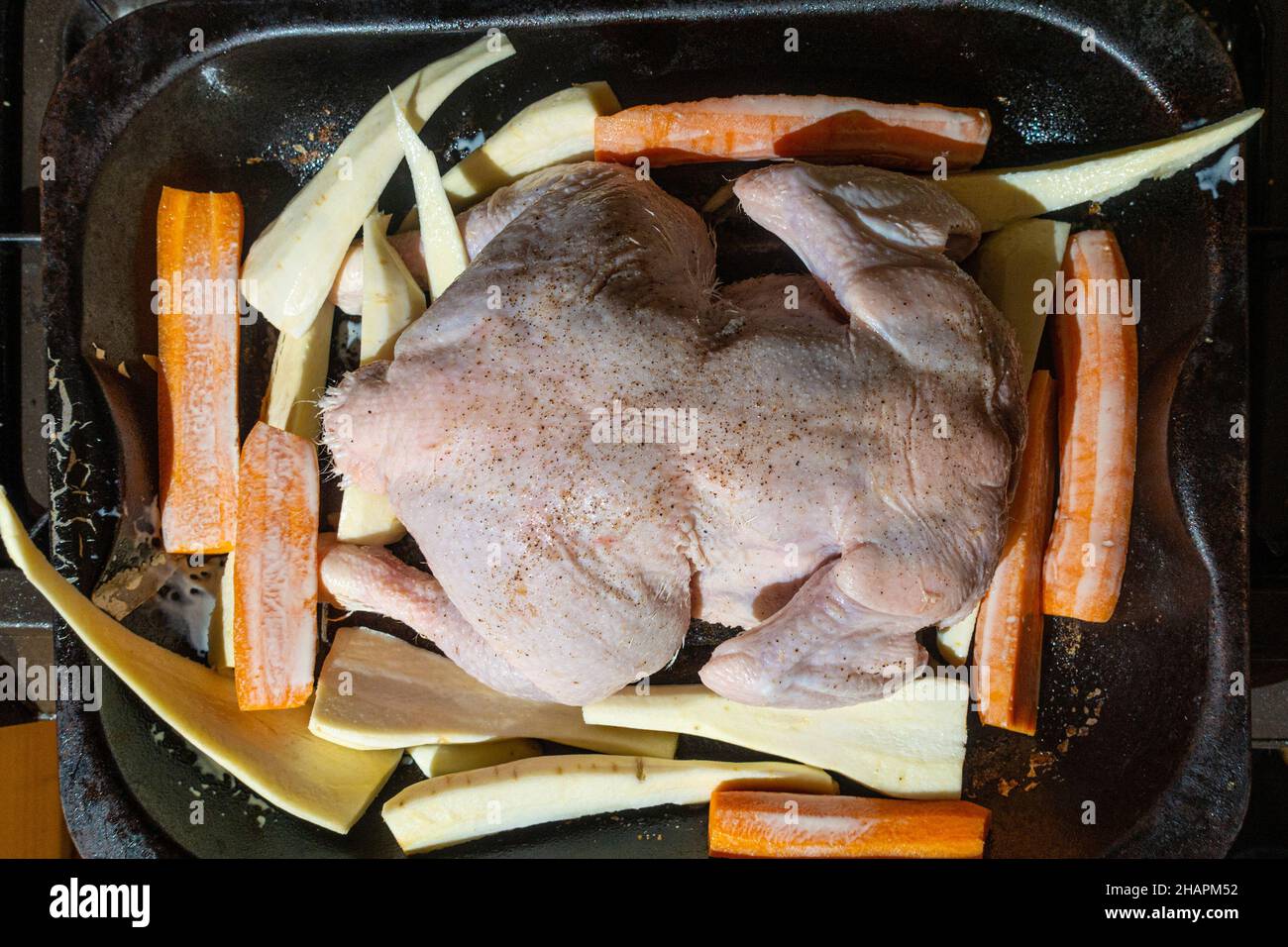 Un pollo in una teglia per arrostire preparato e pronto per il forno, dove verrà arrostito con pezzi di pastinaca e carote a fettine. Foto Stock