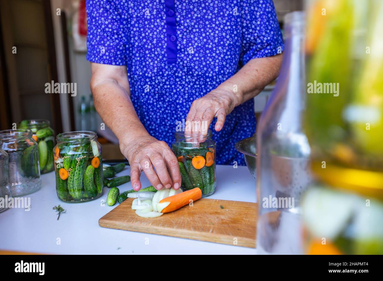 Processo di inscatolamento di un cetriolo, donna anziana inscatolando cetrioli freschi con cipolla e carote, prodotto fatto in casa, concetto di cibo Foto Stock