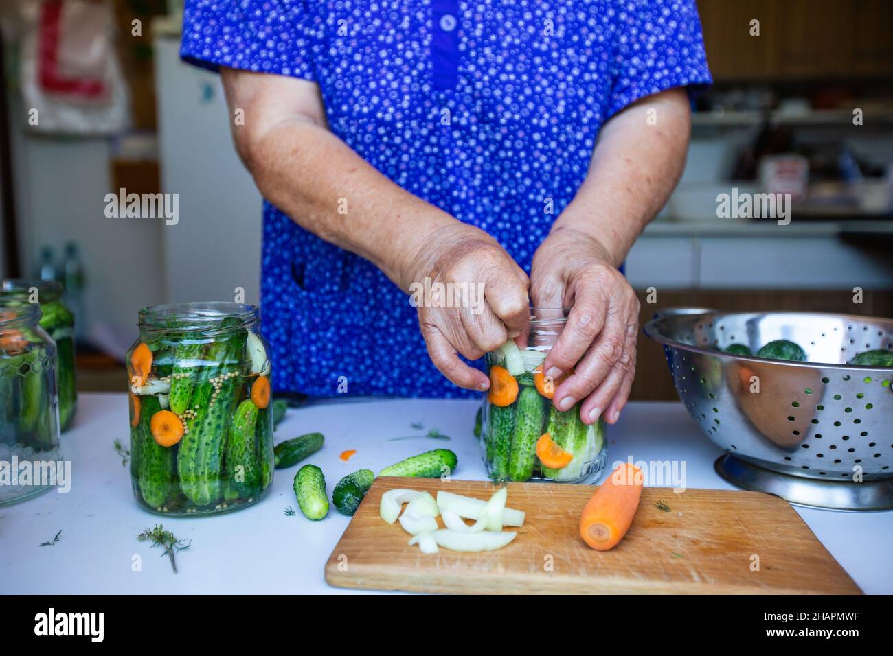Processo di inscatolamento di un cetriolo, donna anziana inscatolando cetrioli freschi con cipolla e carote, prodotto fatto in casa, concetto di cibo Foto Stock