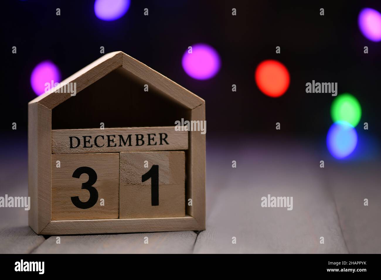 Decorazioni natalizie su sfondo ligneo: Cubetti di legno con i numeri di dicembre 31, e ghirlanda sfumata multicolore sullo sfondo. Selettivo Foto Stock