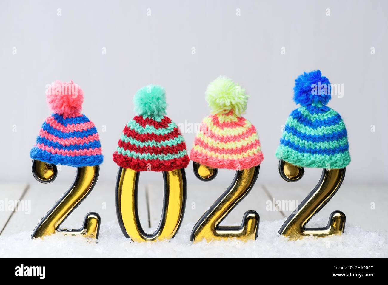Oro Numbers 2022 con cappelli in maglia multicolore su sfondo bianco con neve. Nuovo anno di sfondo con 2022 anni Foto Stock