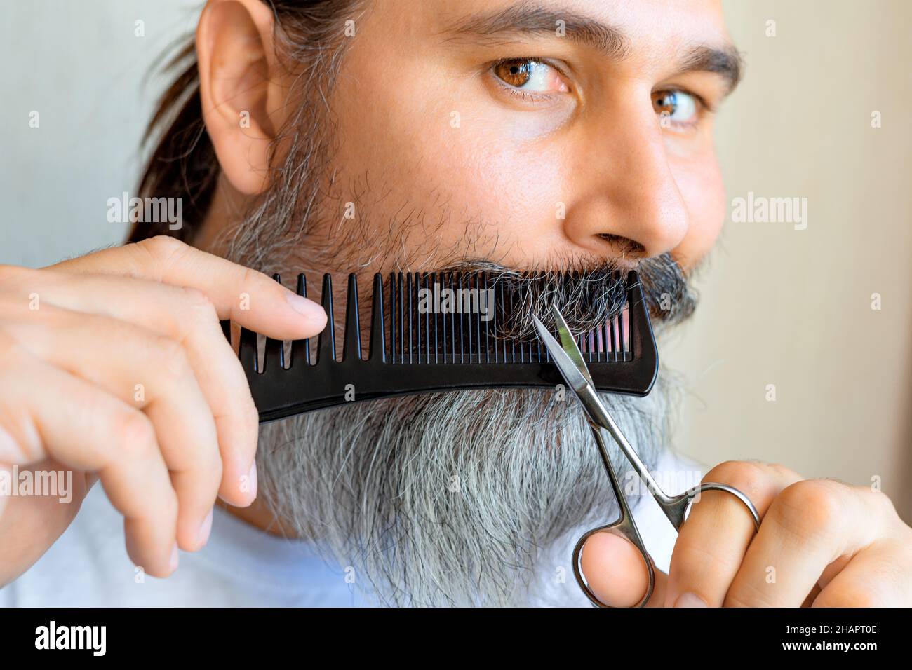 L'uomo caucasico di mezza età tagliò i baffi. Un uomo con baffi grigi taglia i propri baffi utilizzando un pettine e delle forbici. Messa a fuoco selettiva. Foto Stock