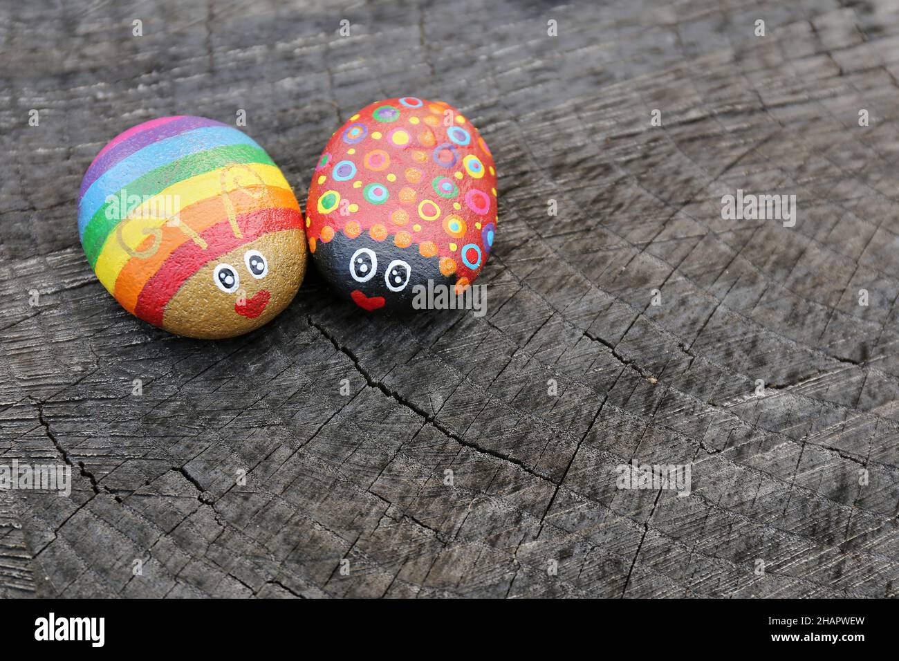 Due insetti di amore arcobaleno dipinti a mano sulle rocce sono seduti su uno sfondo di legno naturale. Foto Stock