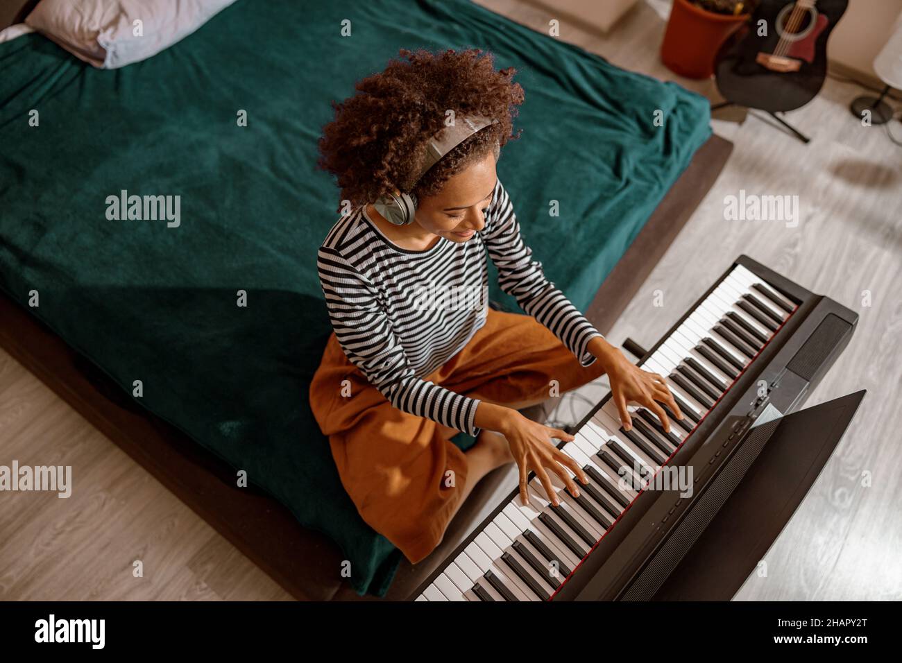 Musicista femminile in cuffie che suona sintetizzatore a casa Foto Stock