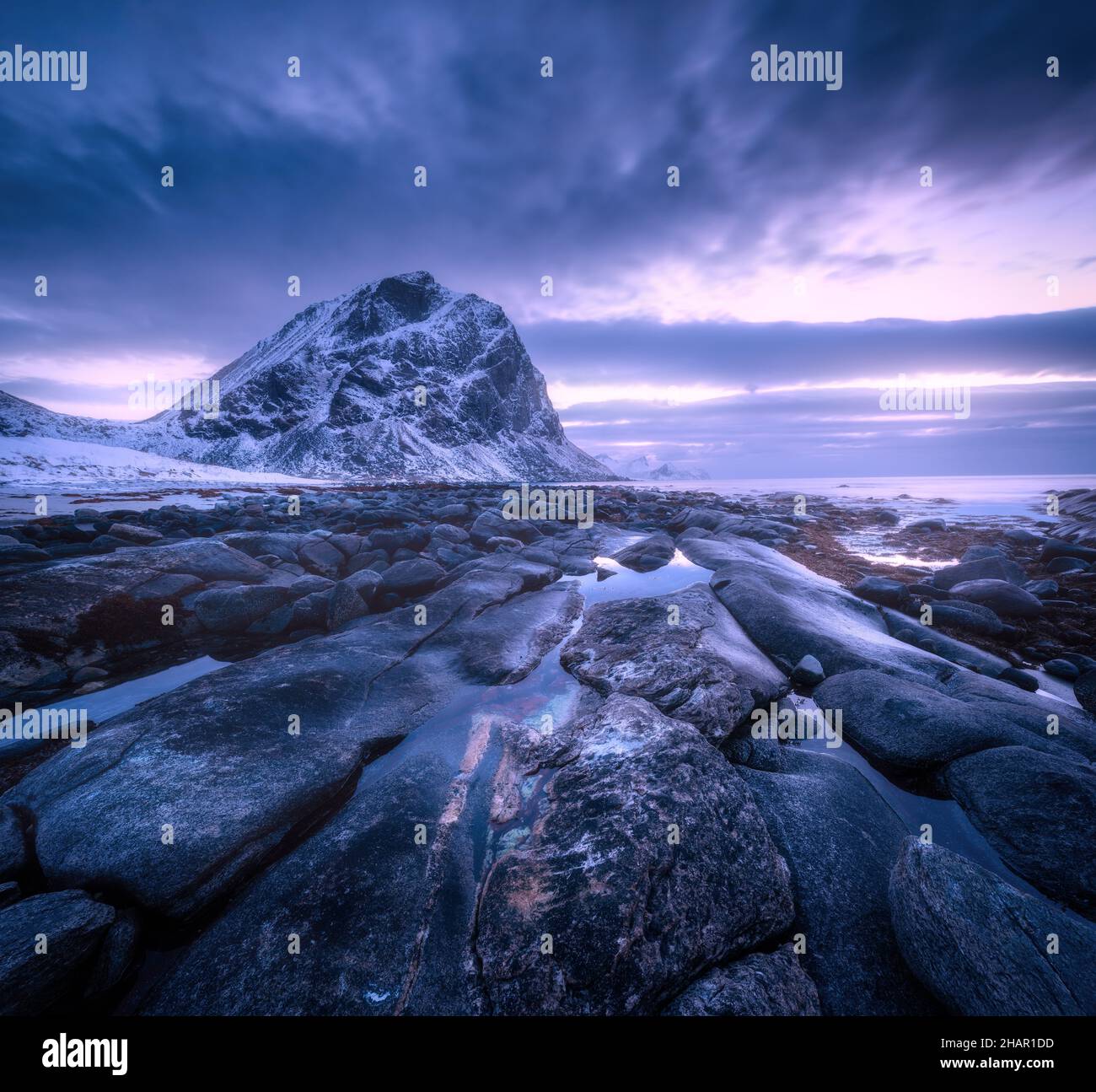 Mare con pietre e acqua sfocata, contro montagne innevate Foto Stock