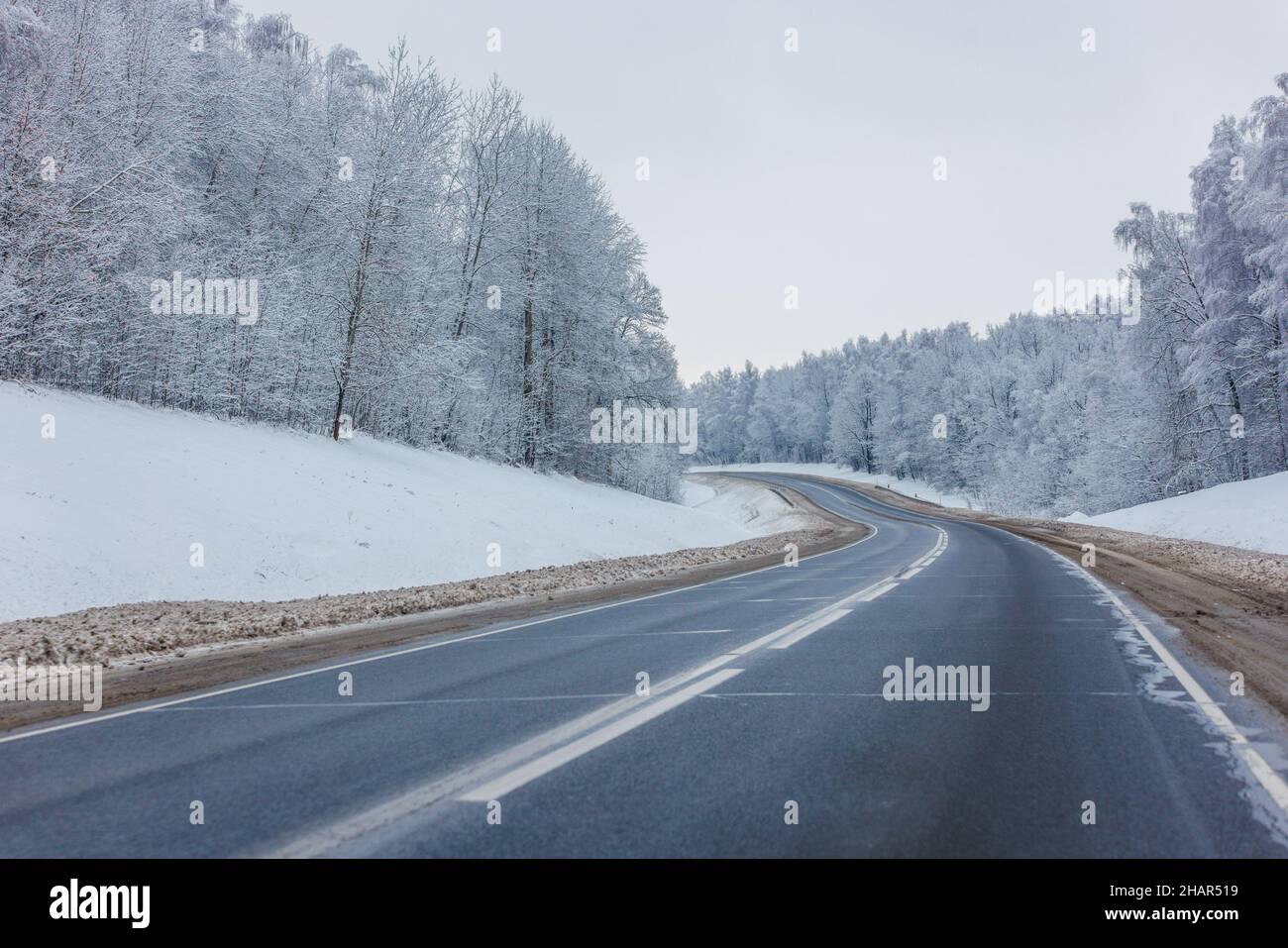 strada invernale vuota tra la foresta ghiacciata alla luce del giorno senza automobili su di essa Foto Stock