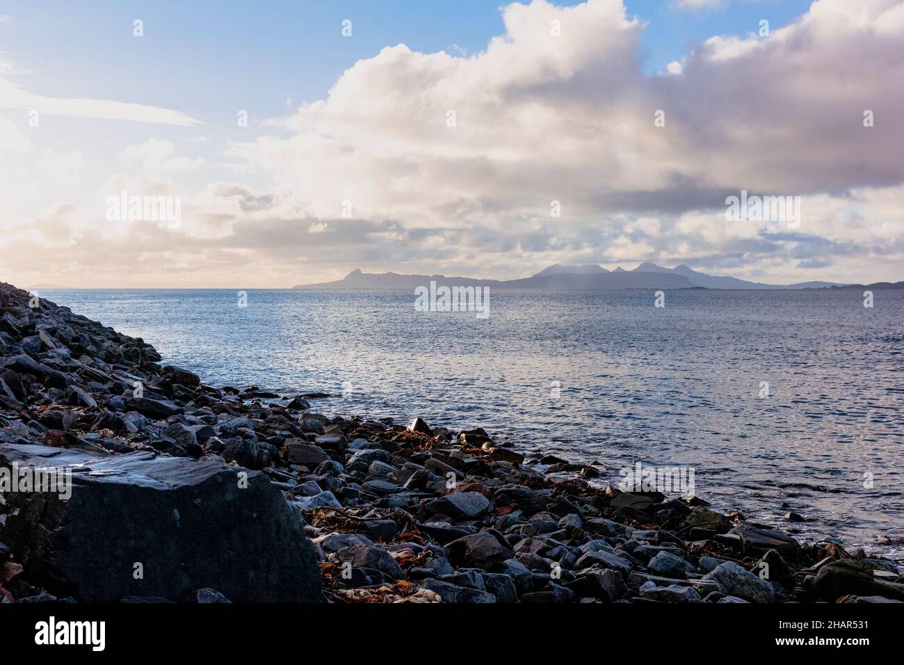 Vista sulle piccole isole di Eigg e Rum sopra il suono di Arisnaig da una spiaggia rocciosa vicino Glenuig, Moidart, sulla costa occidentale della Scozia Foto Stock