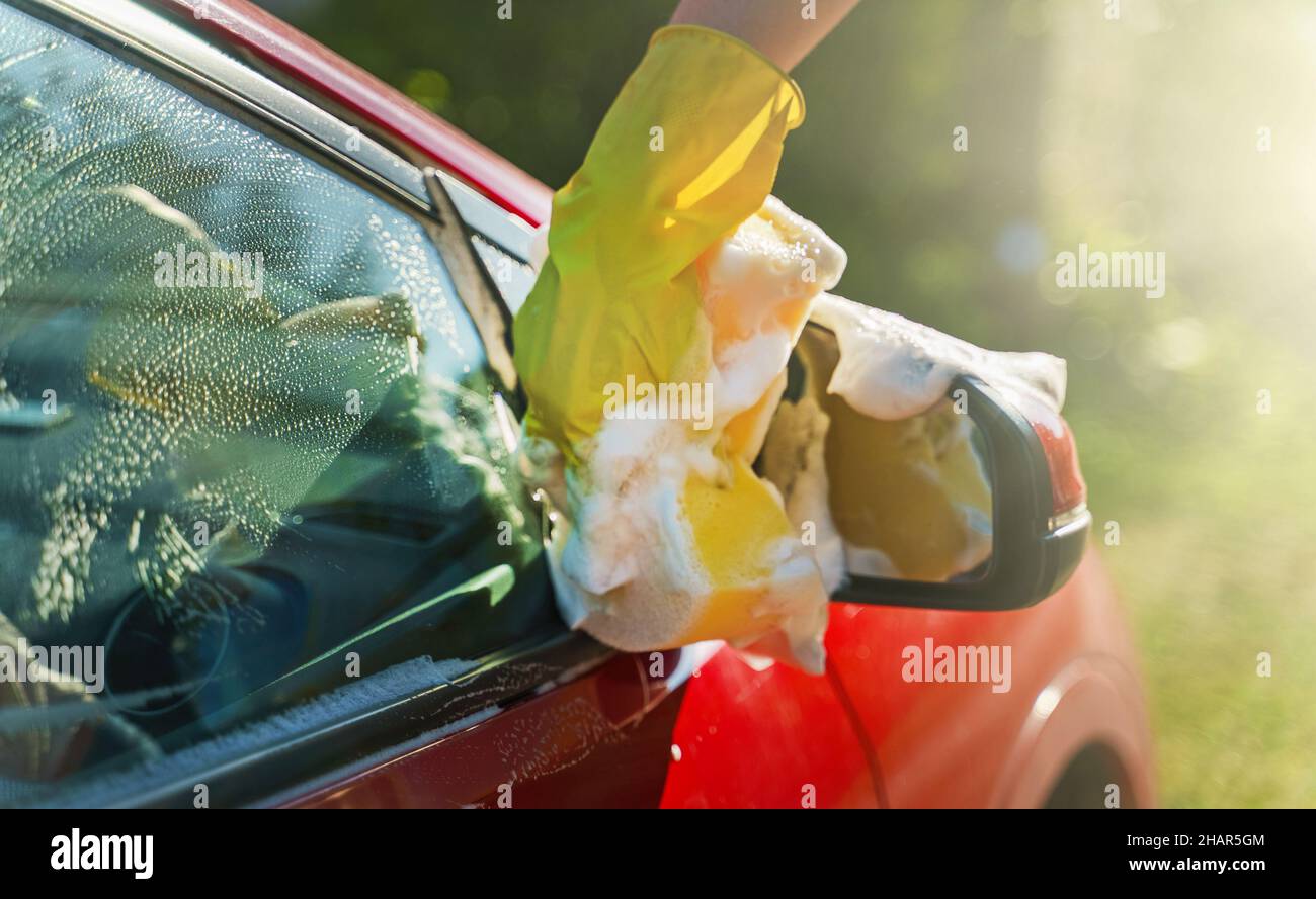 Donna in guanti lava lo specchietto retrovisore con spugna. Foto Stock