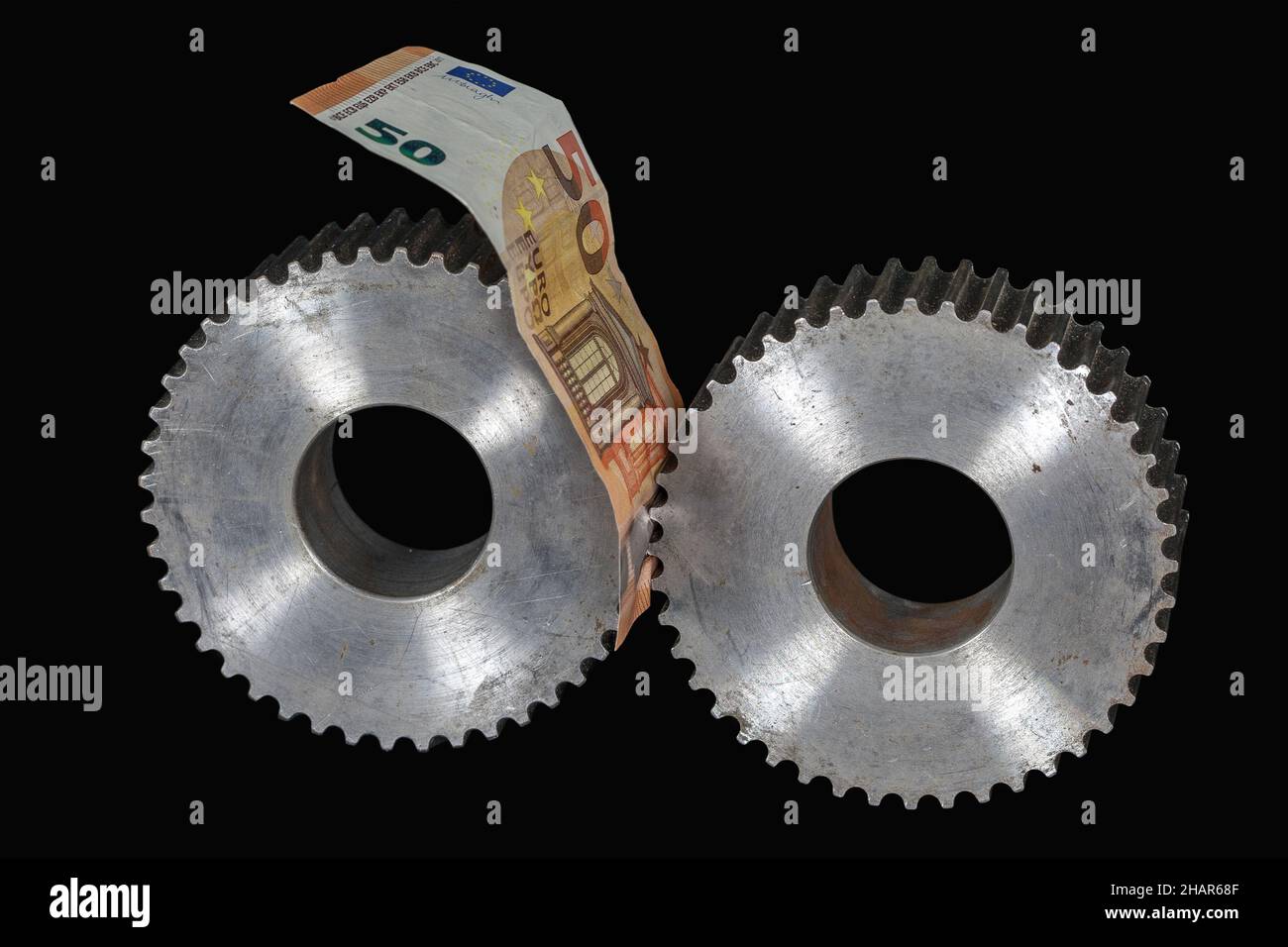 Una nota di cinquanta euro tra due ruote dentate. La moneta europea è compresa tra la politica monetaria a tasso di interesse zero e l'inflazione. Foto Stock