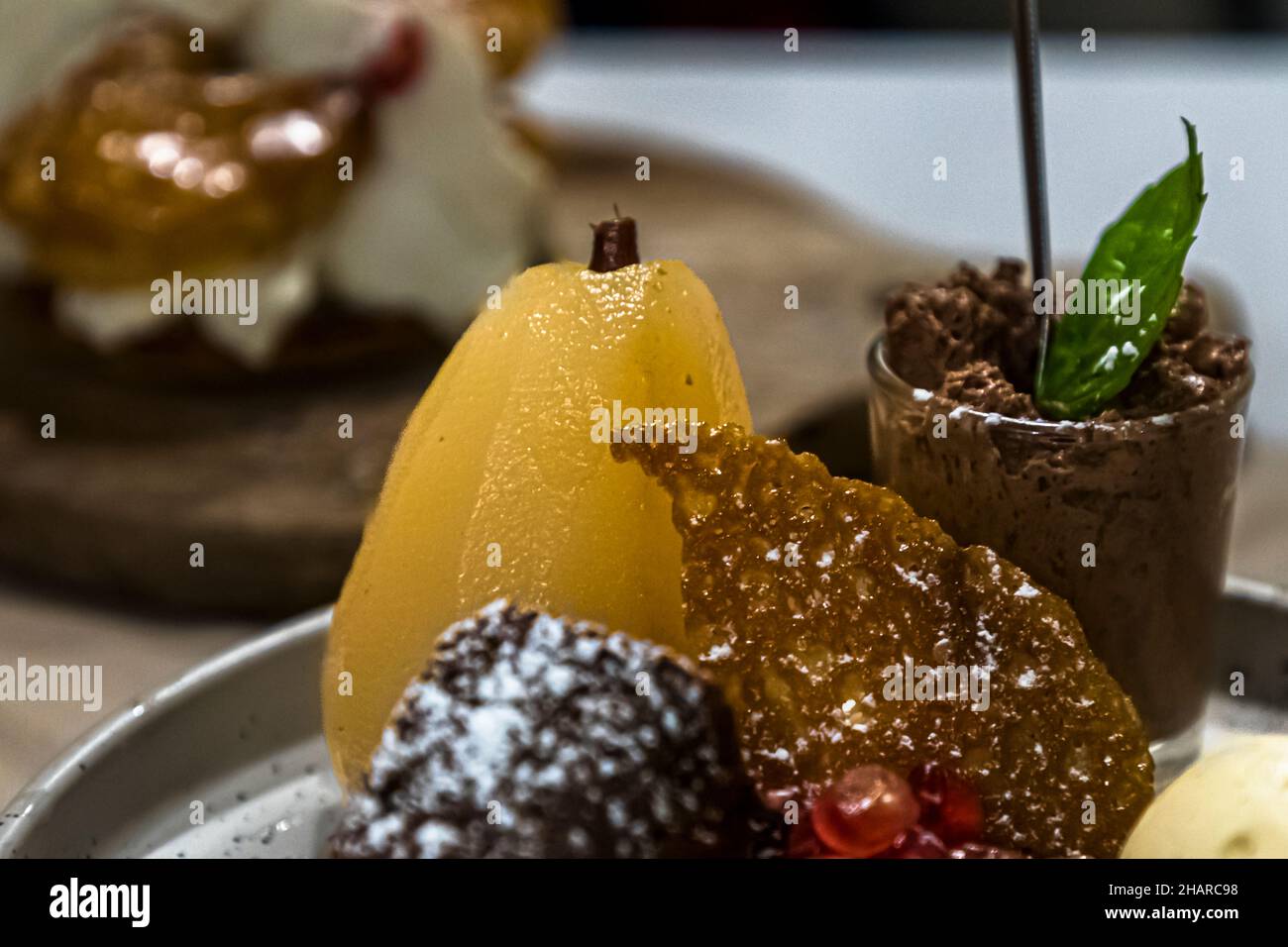 Una pera pochée, un bicchiere di mousse al cioccolato e una confezione di cioccolato spolverata di zucchero a velo sono disposti accanto a una tuile al caramello su un piatto da dessert al ristorante Saint Marc ad Aups, nel dipartimento della Var, Francia. Foto Stock