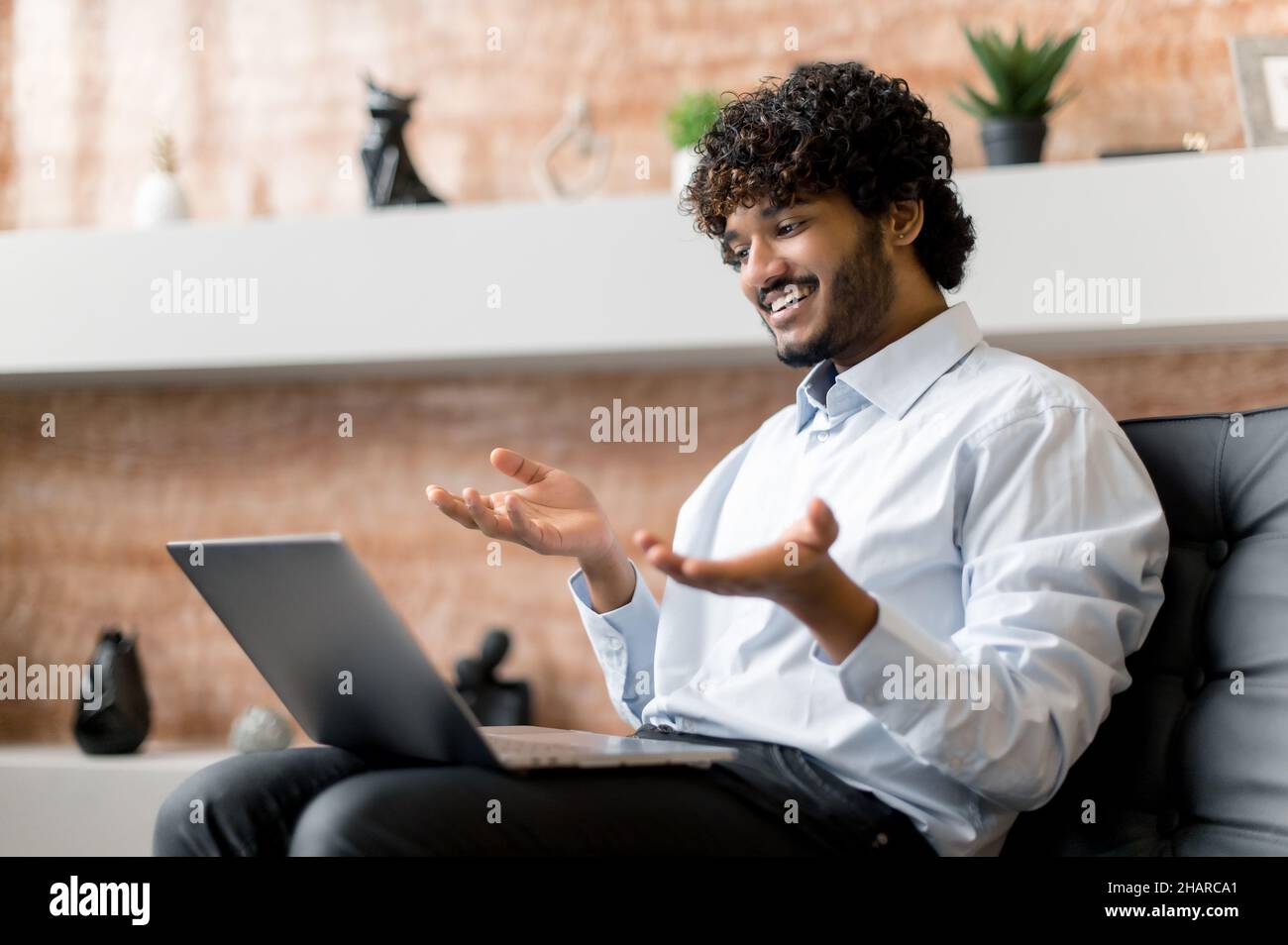 Amichevole positivo giovane adulto indiano business man o freelance con barba, utilizzando il portatile, parlando via video comunicazione con amici, colleghi o la famiglia. Video meeting online, comunicazione virtuale Foto Stock
