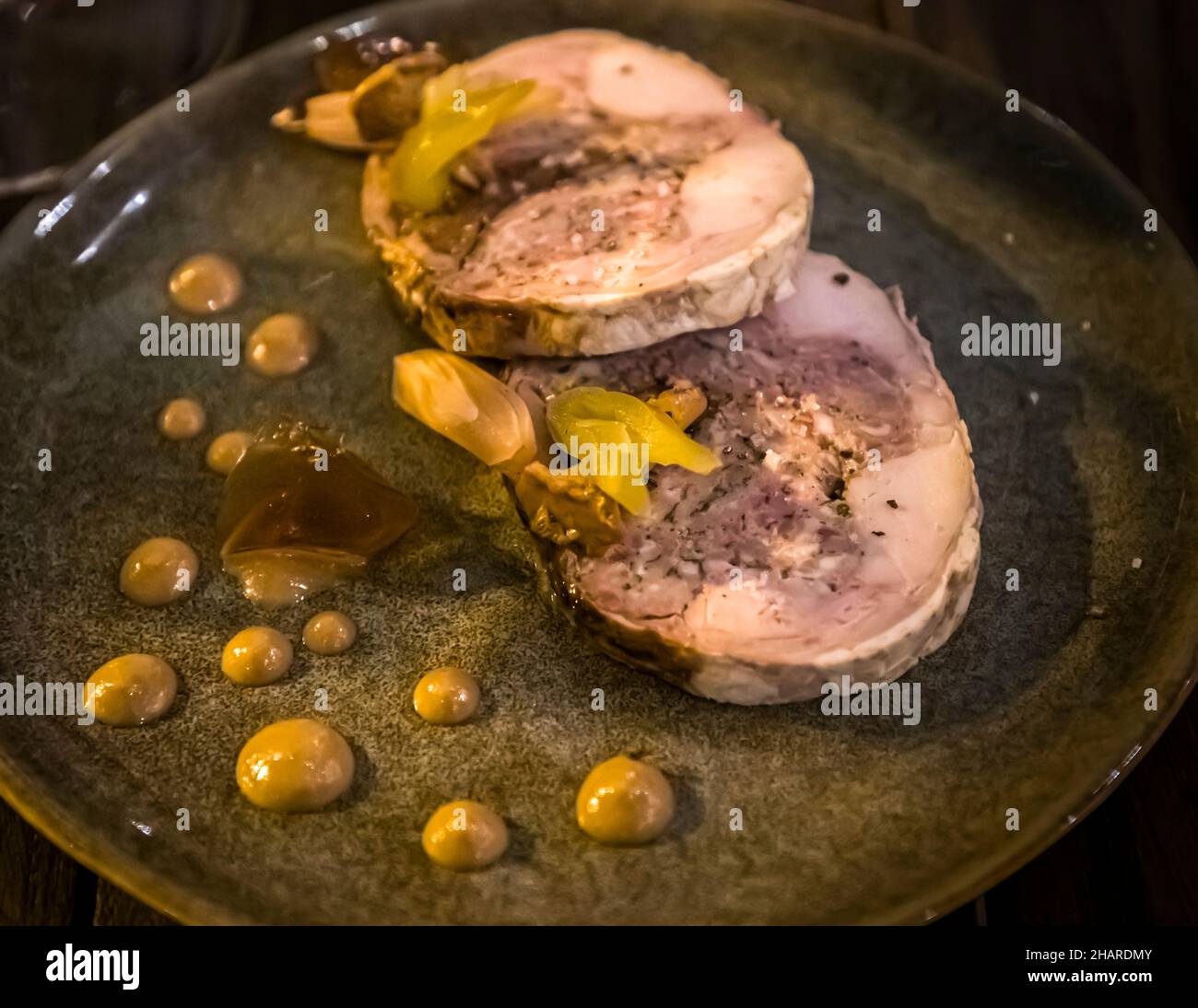 Rotoli di carne pallida, probabilmente maiale o vitello, giacciono con macchie di senape e piccole cipolle sottaceto su un piatto verde scuro al Restaurant Hestia a Bormes-les-Mimosas, dipartimento di Var, Francia. Foto Stock