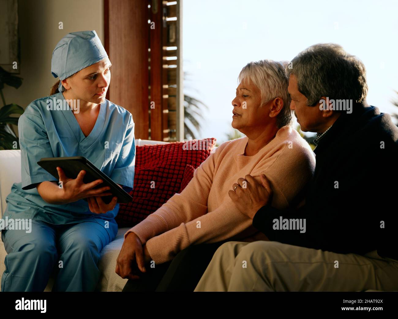 Medico che spiega la diagnosi a coppie anziane multietniche in consultazione a casa Foto Stock