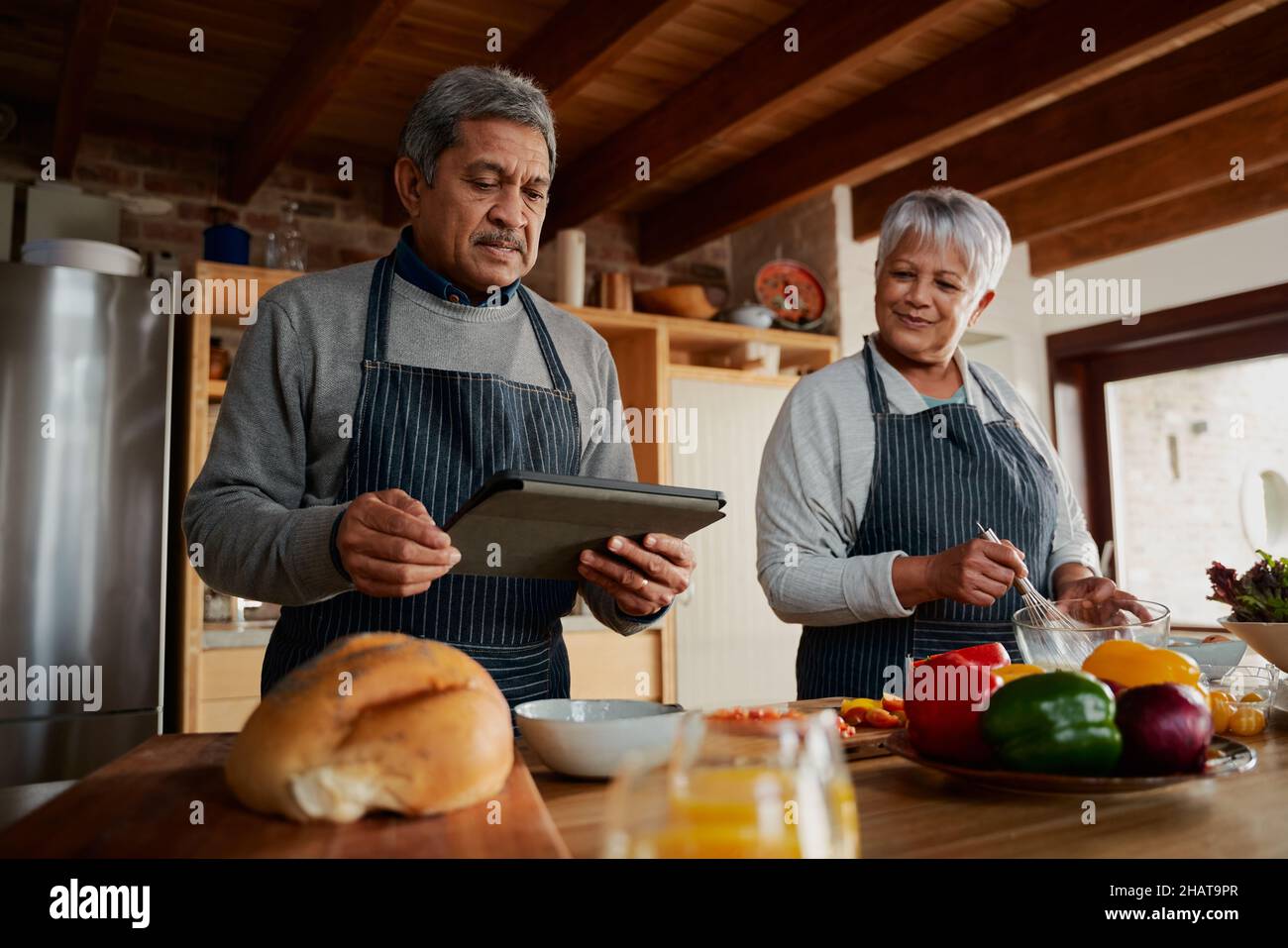 Coppia multiculturale anziani seguendo ricetta su tavoletta elettronica per cucinare pasto sano in cucina moderna. Foto Stock