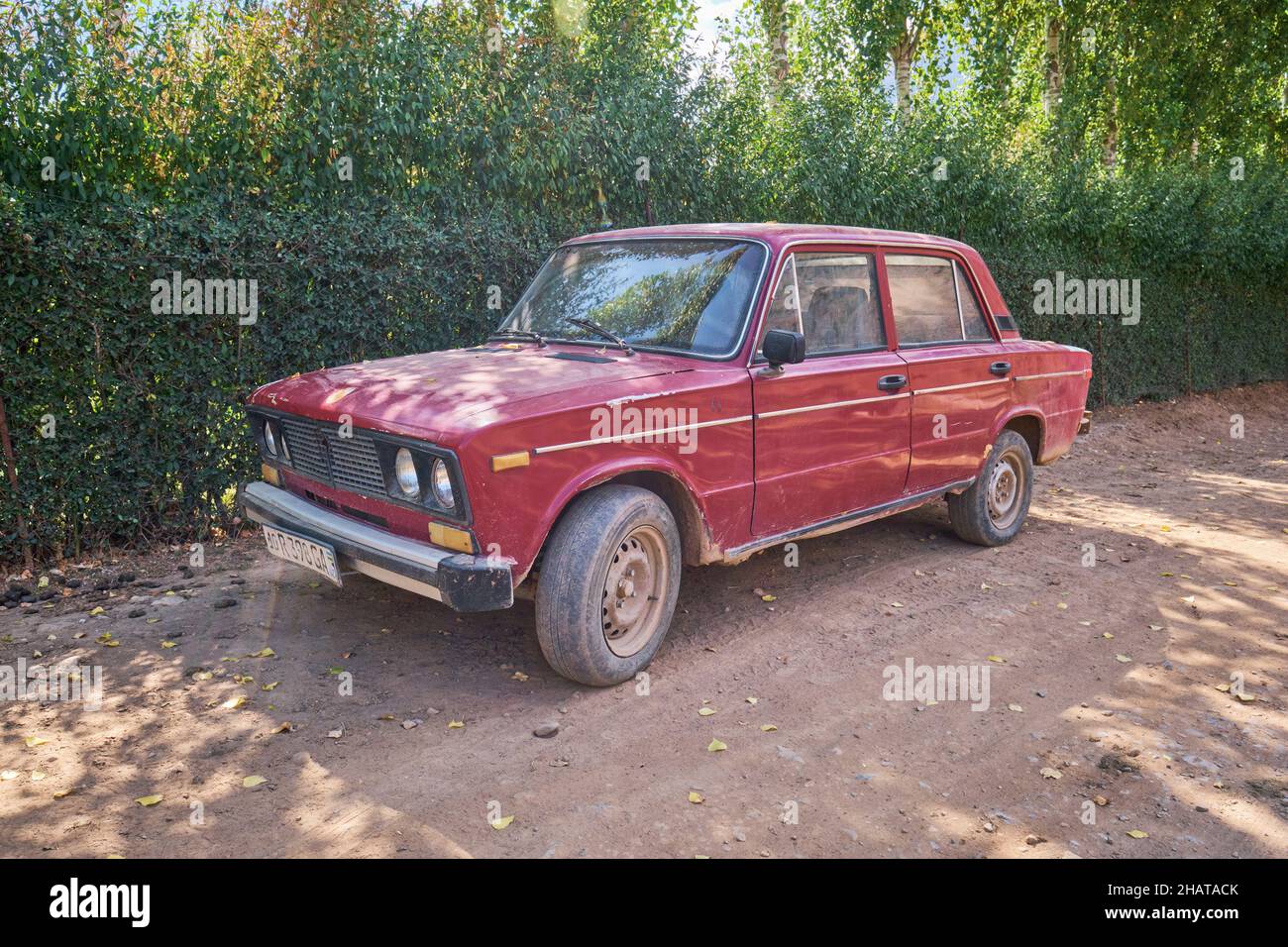Una vecchia macchina rossa russa Lada parcheggiata su una polverosa strada rurale del paese. Nella zona del lago Charvak resevoir vicino Tashkent, Uzbekistan. Foto Stock