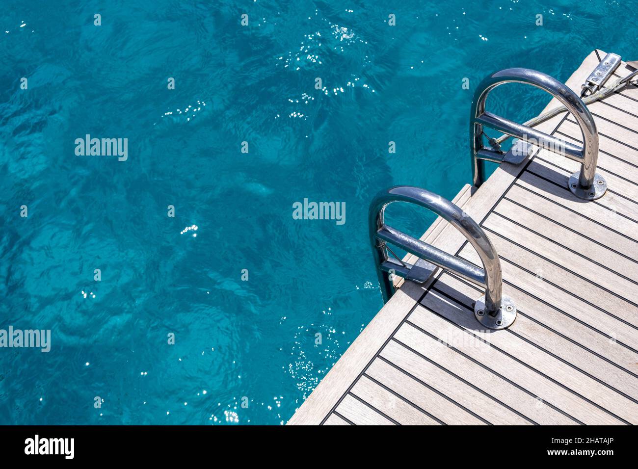 Ponte sul retro della barca, scale in legno di teak e metallo, sfondo blu dell'acqua di mare. Crociera in yacht di lusso, mar Egeo Grecia Foto Stock