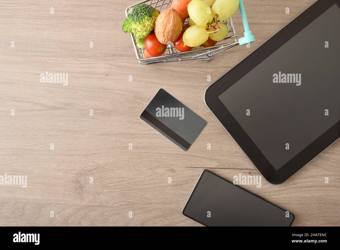 Concetto di shopping online con dispositivi mobili e mini supermercato carrello pieno di frutta e verdura su tavola di legno. Vista dall'alto. COM. Orizzontale Foto Stock