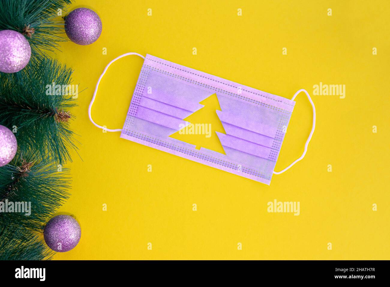 Maschera medica viola o molto peri con silhouette ritagliata dell'albero di Natale su sfondo giallo.rami dell'albero di Natale vicino alla maschera. Natale e Felice anno nuovo nel concetto di coronavirus Foto Stock