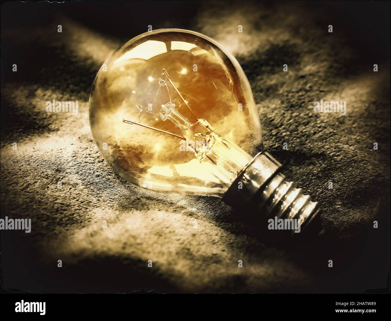 Primo piano di una singola lampadina dorata che illumina la luce, con montaggio a vite su uno sfondo a chiazze in uno stile vintage scuro e moody desaturato Foto Stock