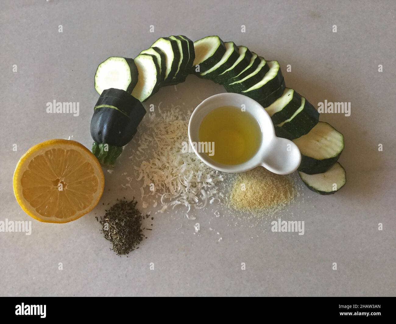 Zucchine a fette poste in un anello, limone dimezzato, olio d'oliva in ciotole, parmigiano grattugiato Foto Stock