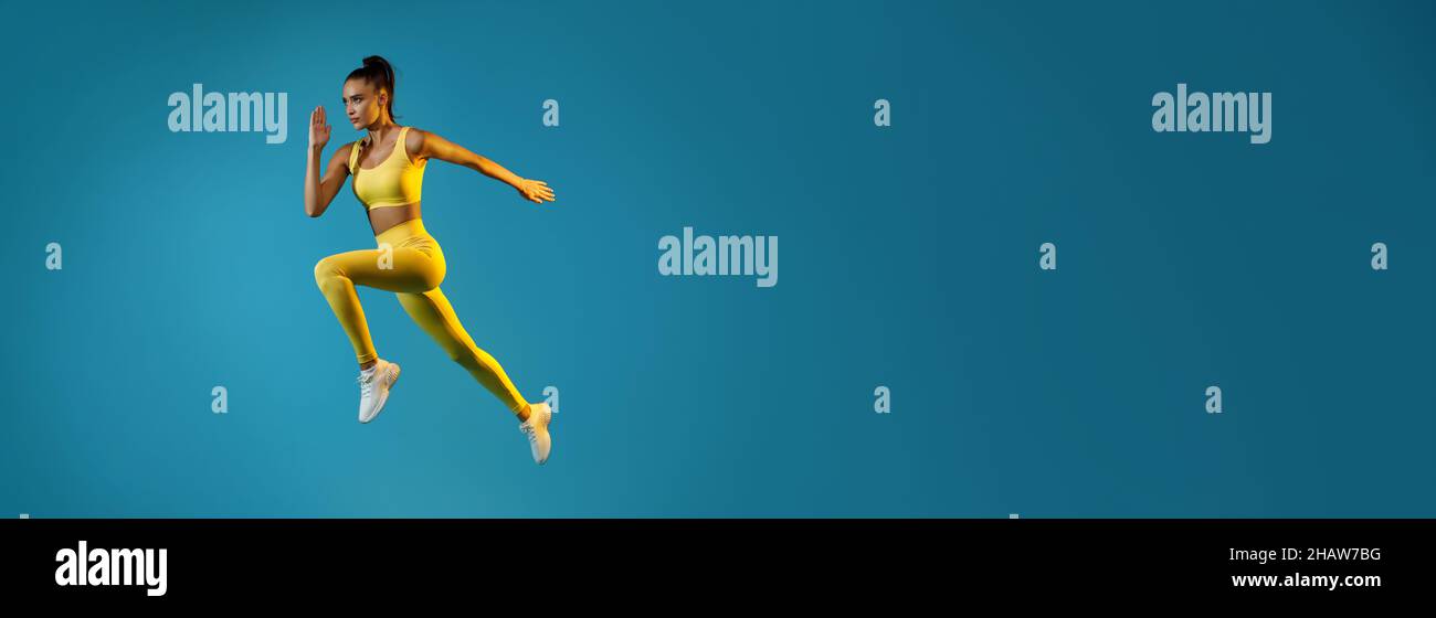 Atletica femmina saltando in mezzo-aria guardando da parte, sfondo blu Foto Stock