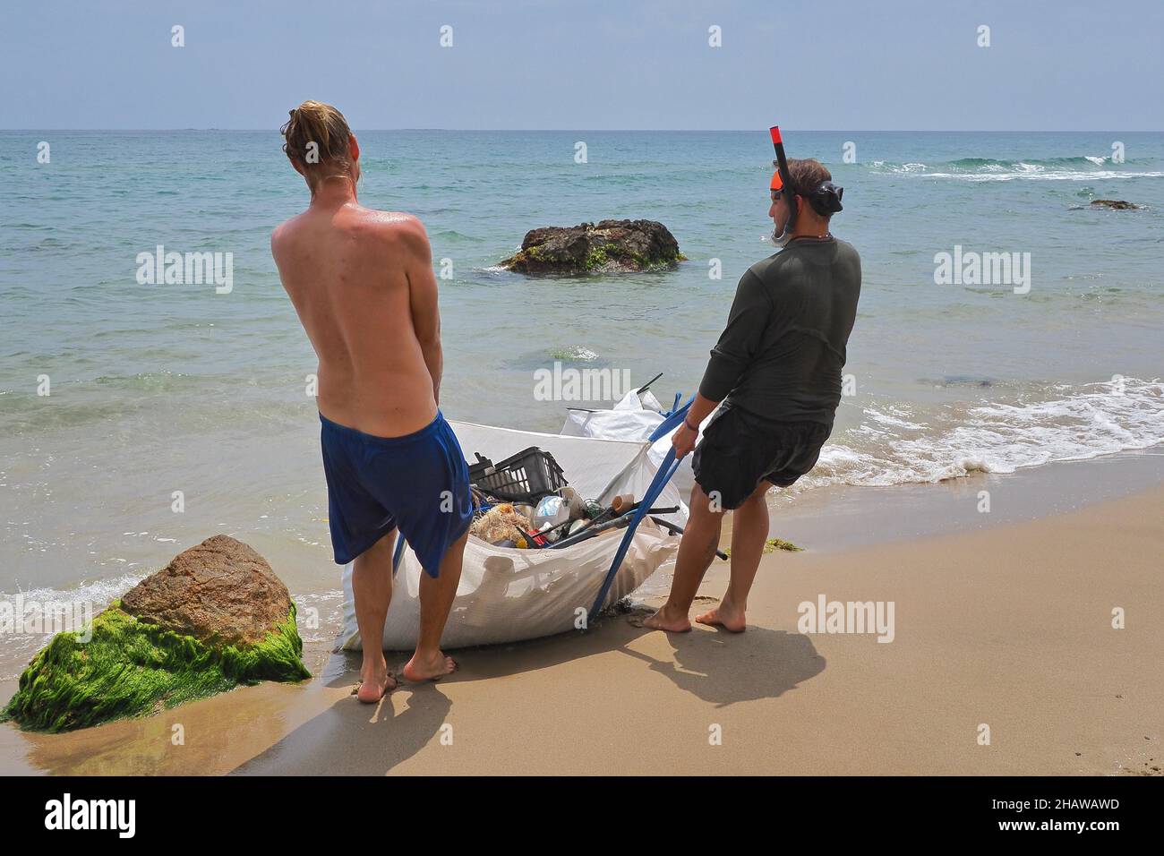 Due giovani uomini sulla spiaggia tirando pesante sacco di rifiuti di plastica, pulizia spiaggia, Almeria, Andalusia, Spagna Foto Stock