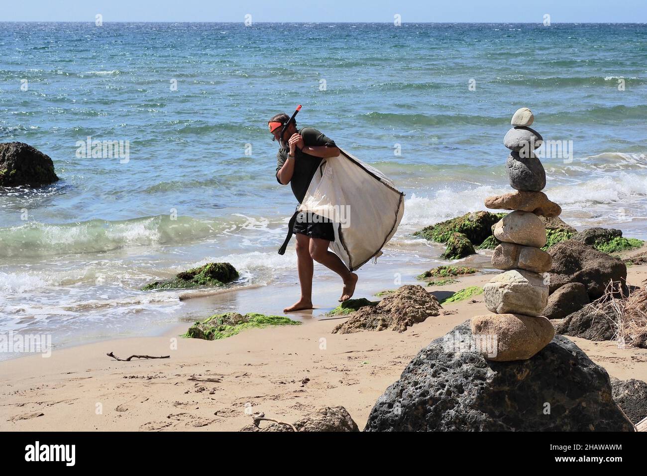 L'uomo in maschera subacquea trascina un sacco pesante di rifiuti di plastica, pulizia della spiaggia, Almeria, Andalucia, Spagna Foto Stock