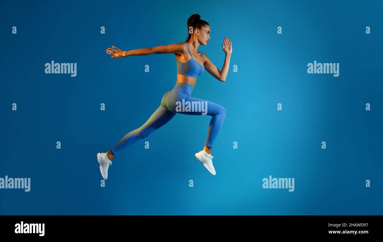 Determinato giovane Sportswoman saltare in posa a metà aria su sfondo blu Foto Stock