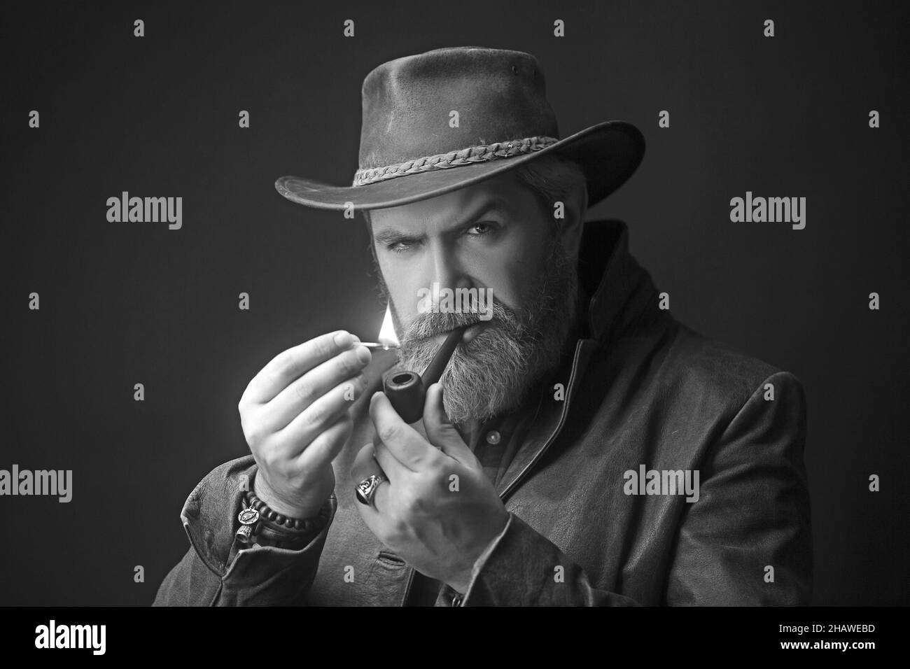Il giovane uomo brutale ed elegante fuma una pipa sul luogo oscuro. Foto Stock