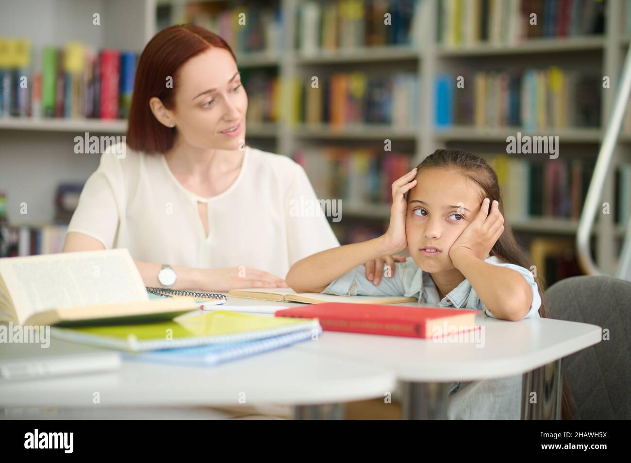 Donna che guarda interrogatamente a ragazza stanca che studia a tavola Foto Stock