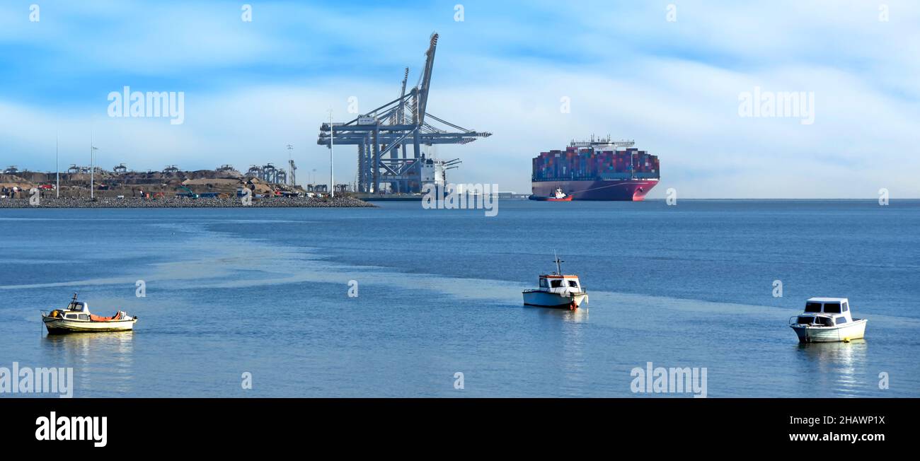 Tugboat che tira la nave grande del contenitore & il carico pieno dei contenitori di trasporto alla nascita sotto le gru alte giganti a porta estuario del Tamigi di Londra Essex Regno Unito di Gateway Foto Stock