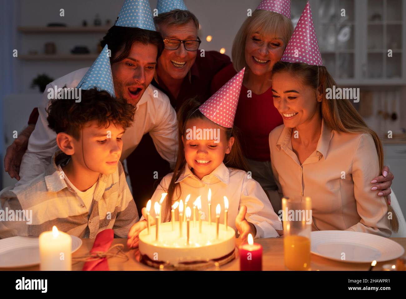 Carina bambina che riceve la torta di compleanno yummy con candele accese per il compleanno, festeggiando la vacanza con la famiglia estesa Foto Stock