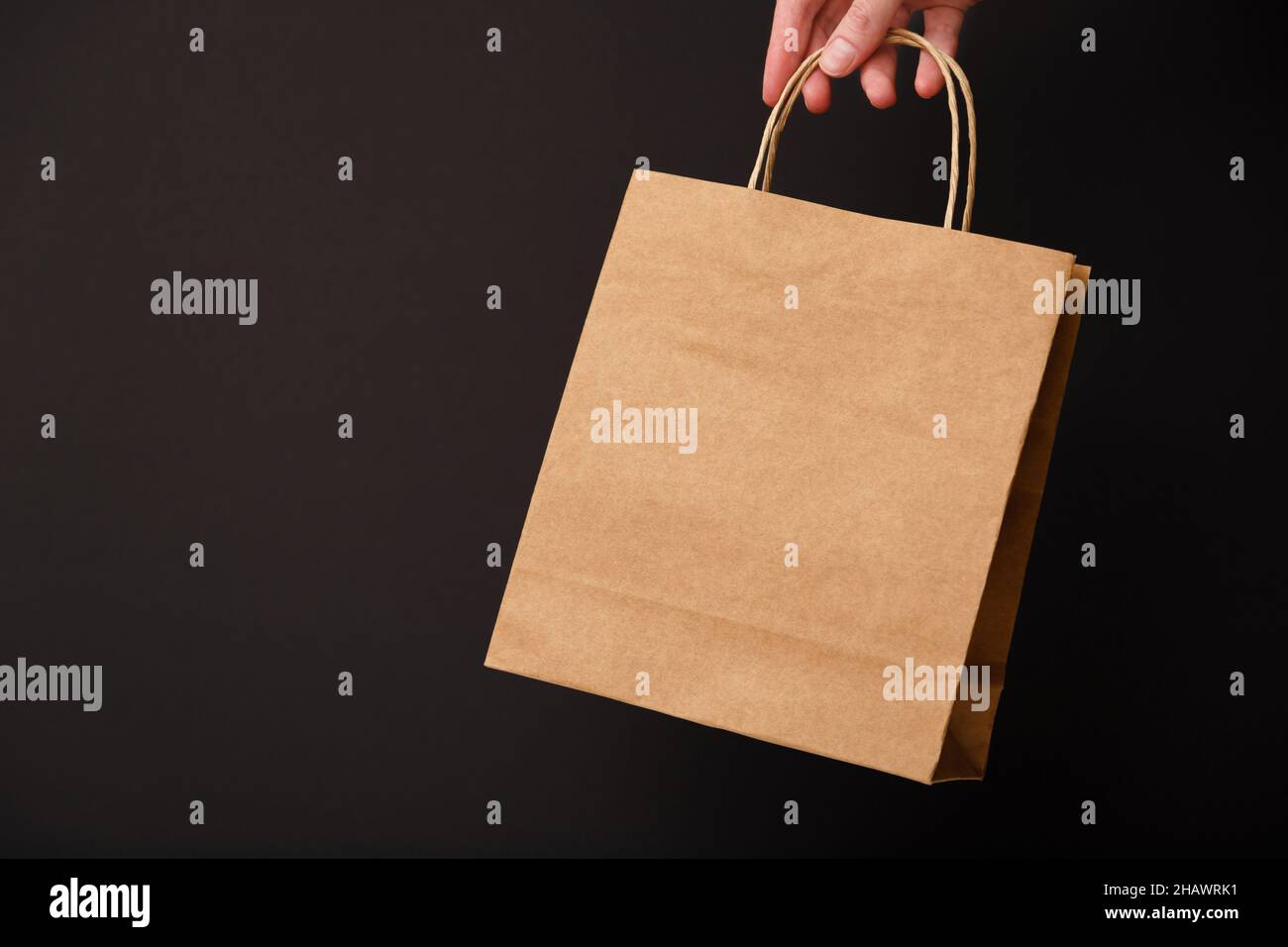 Donna mano che tiene bruno mestiere bianco shopping bag isolato su sfondo nero. Vendita del black friday, sconto, riciclaggio, shopping e concetto di ecologia Foto Stock