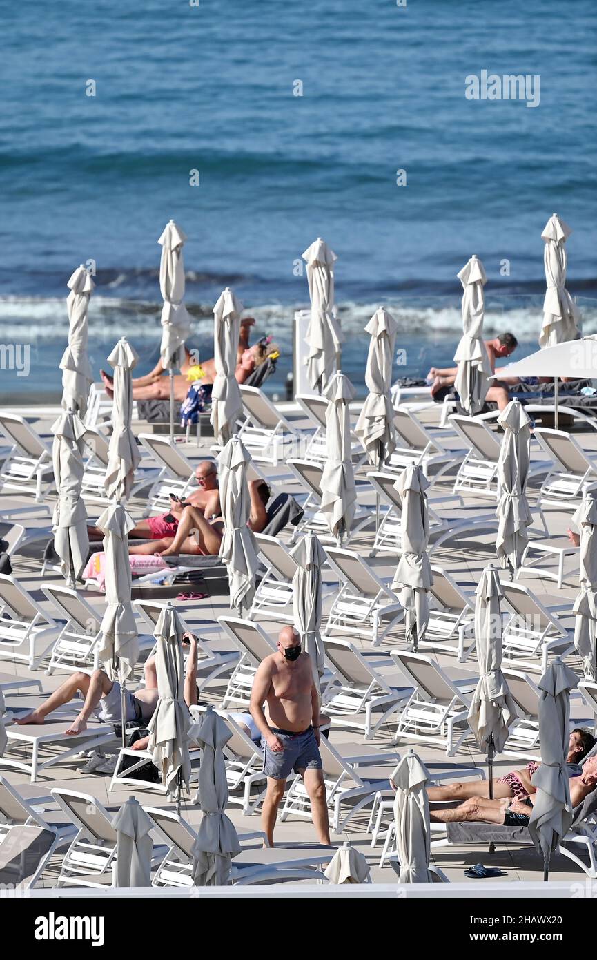 I vacanzieri che indossano maschere protettive per proteggere contro Covid-19 sono visti dai lettini di un hotel a Tenerife, Spagna. Dicembre 2021. Foto Stock